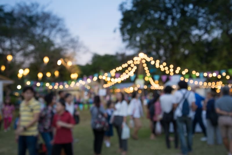 Participantes de evento confraternizando em área aberta arborizada e decorada com luzes