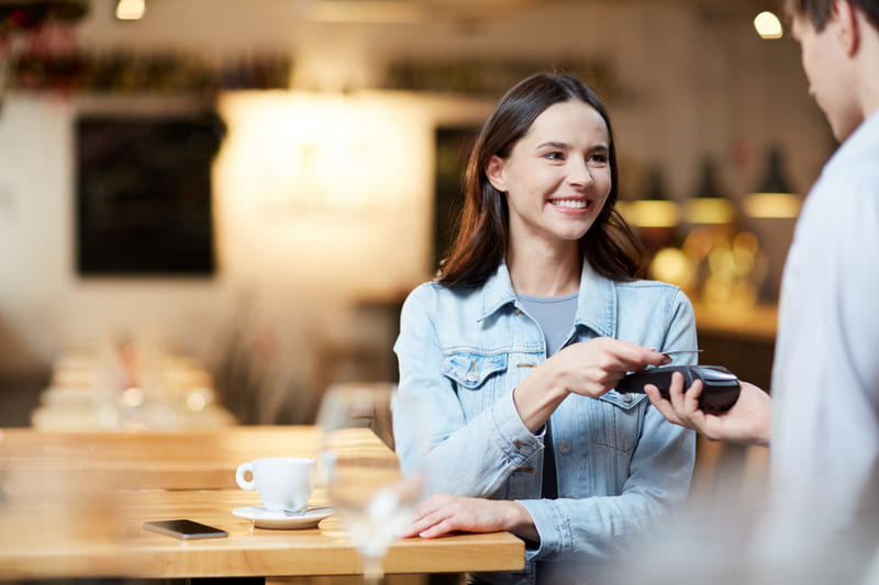 Cliente sentada sozinha em mesa de cafeteria realiza pagamento por aproximação na maquininha